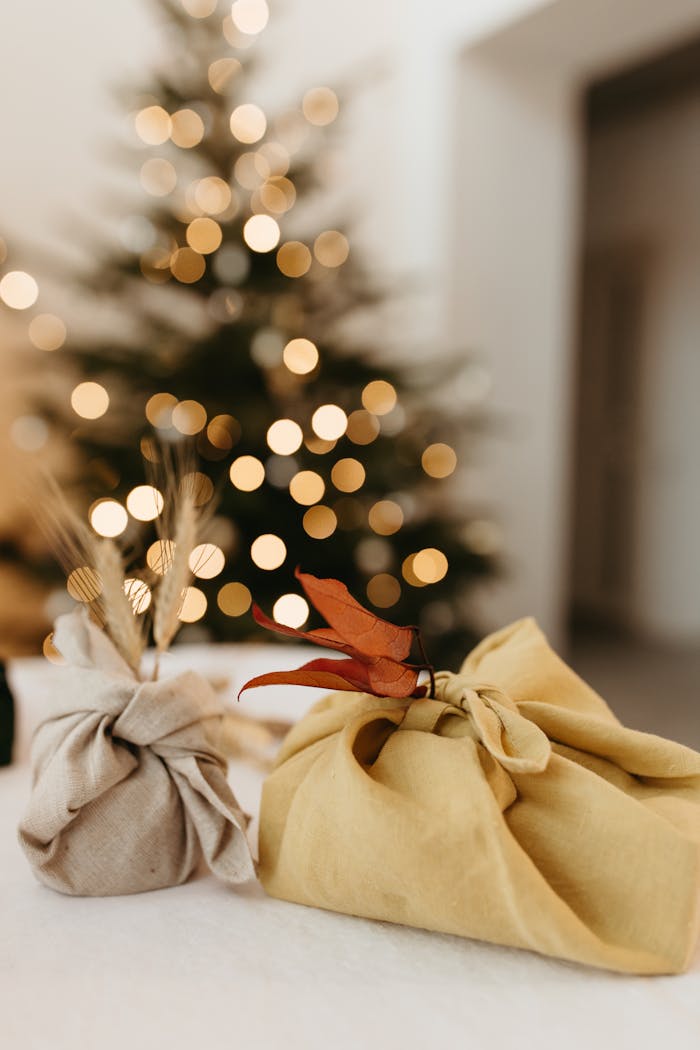Hand-wrapped eco-friendly gifts under a blurred Christmas tree.