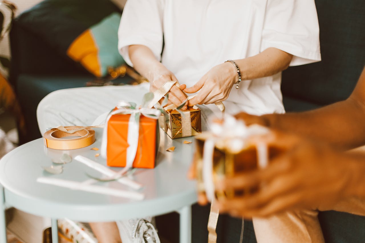 Individuals wrapping gifts, focusing on hands and packages on a table indoors.